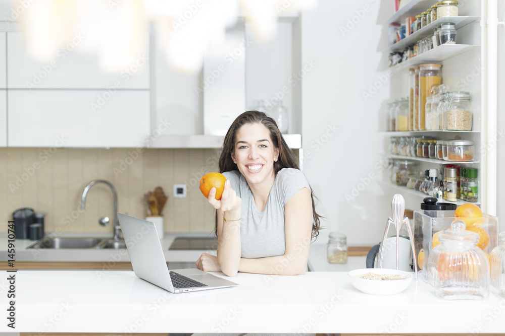 Morning scene. Beautiful woman holding orange in front of laptop Morning scene. Beautiful woman holding orange in front of laptop