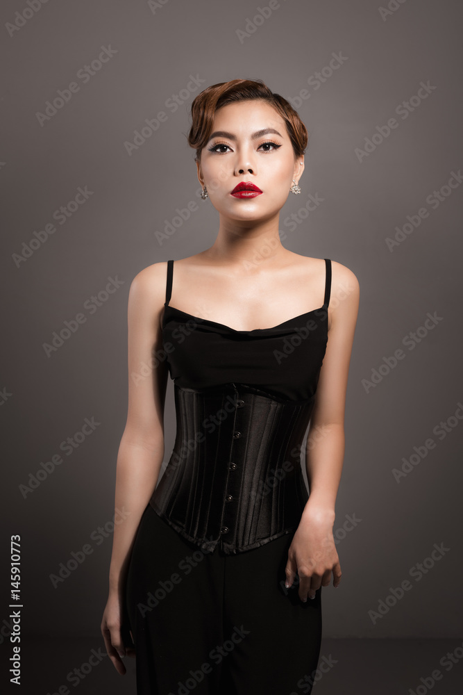 Sexy attractive asian woman posing in fashionable black dress over grey background Sexy attractive asian woman posing in fashionable black dress over grey background