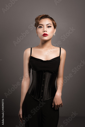 Sexy attractive asian woman posing in fashionable black dress over grey background