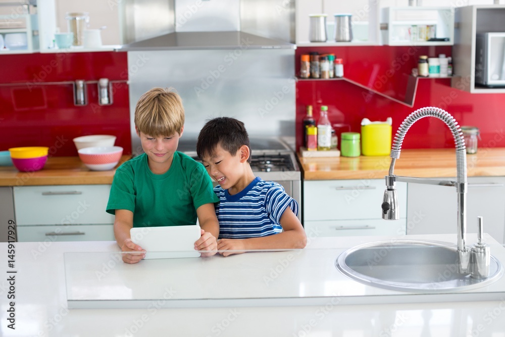 Siblings using digital tablet in kitchen Siblings using digital tablet in kitchen