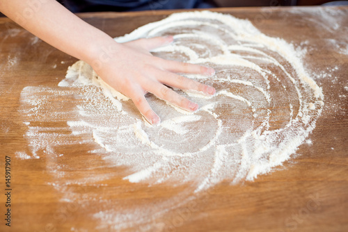 little child making pizza dough on wooden tabletop in kitchen
