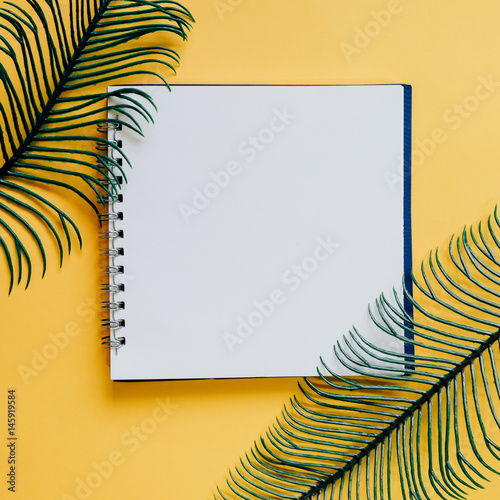 Flat lay of minimal workspace blank notebook with green plant on yellow background, spring and summer concept