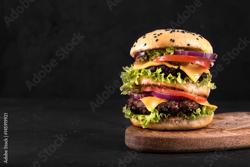Big juicy hamburger with vegetables and beef on black background. Vintage toned
