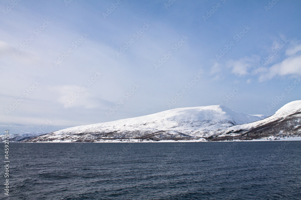 scenic view from boat trip on beautiful snowy fjords in norwegian sea in blue sky, norway