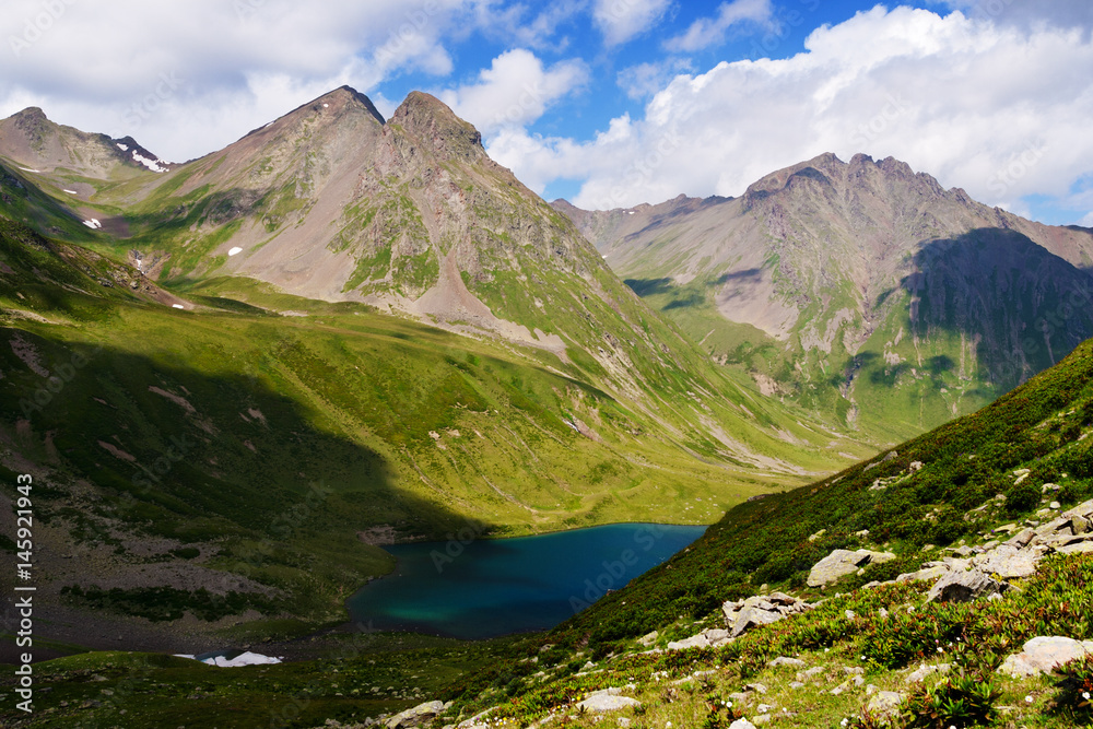 Mountain Lake in the mountains of Western Caucasus. Bright blue sky and white clouds.