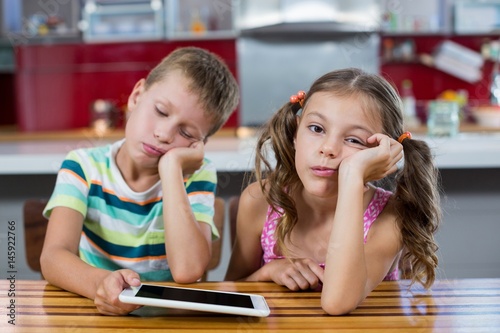 Bored siblings with digital tablet in kitchen photo