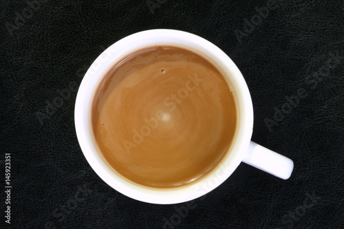 Coffee ready mix in the cup represent cream layer floating on the coffee surface put on black color leather platemat.
