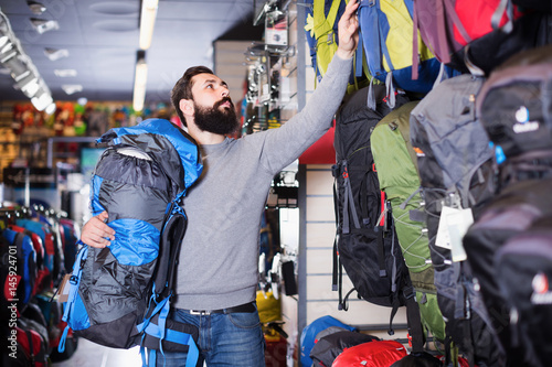Young male choosing new backpack in store