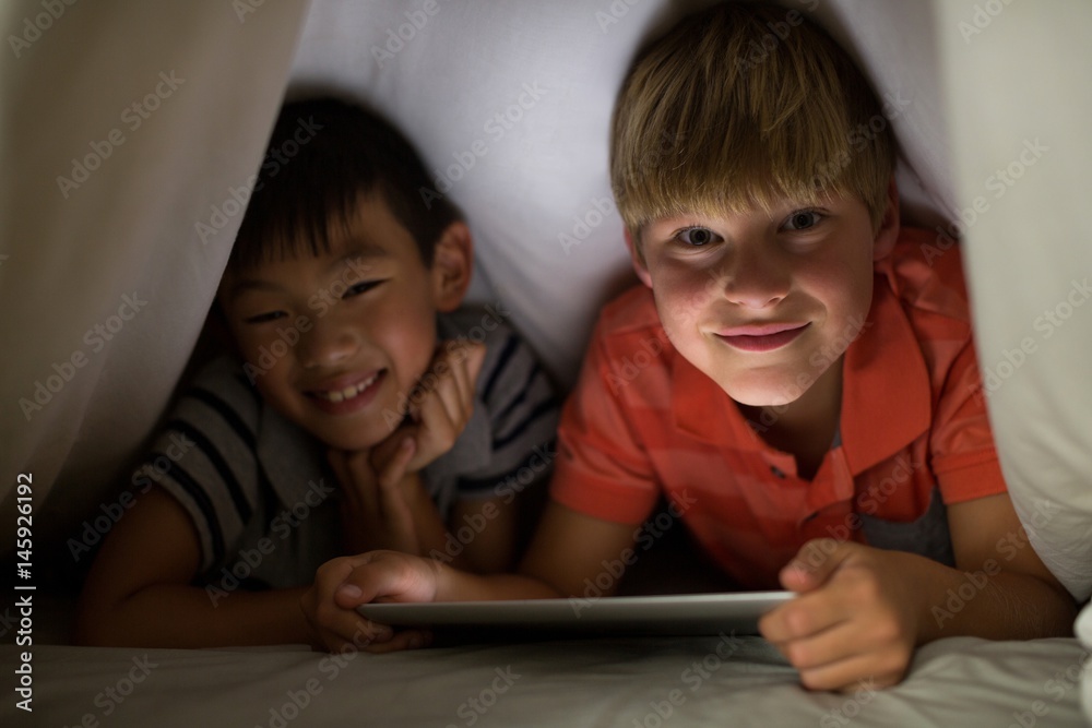 Portrait of siblings under bed sheet using digital tablet on bed Portrait of siblings under bed sheet using digital tablet on bed