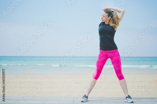 Runner woman stretching hands , stretch exercise . Fitness female athlete relaxing on beach doing a warm-up before running