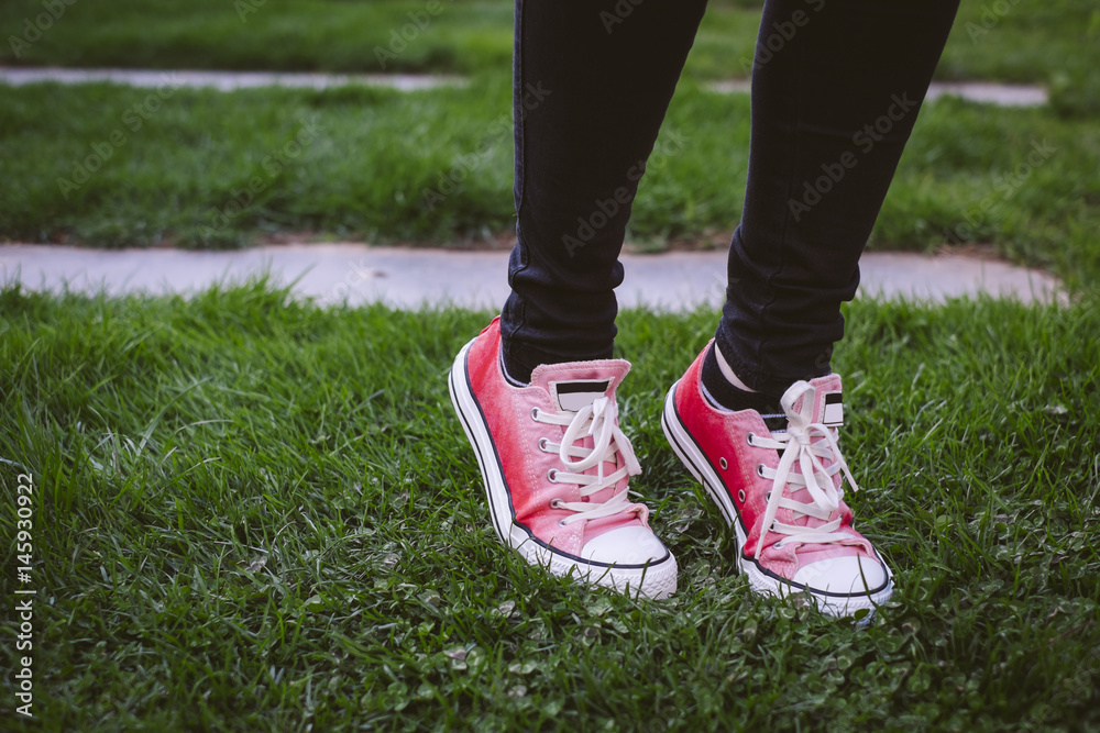 Female shoes on green grass. She is wearing black pants and pink sneakers.