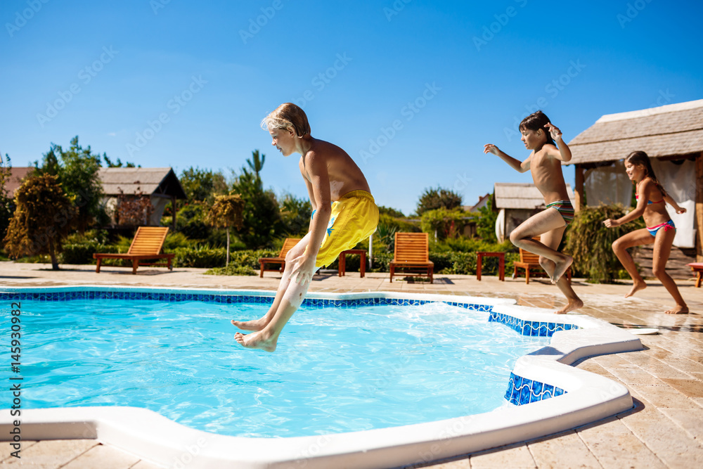 Cheerful children rejoicing, jumping, swimming in pool.