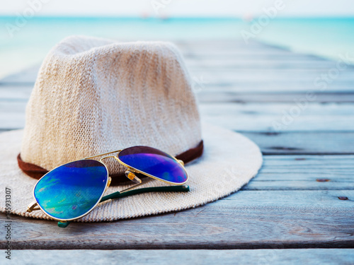 Straw hat and sunglasses on wood bridge against tropical beach background.