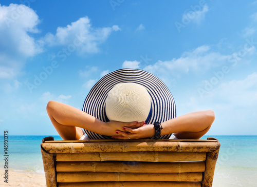 Woman in hat relaxing on beach, looking at sea.