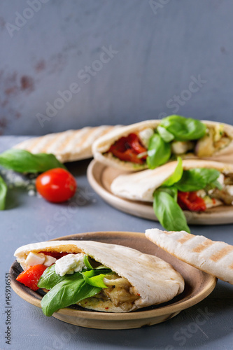 Pita bread sandwiches with grilled vegetables paprika, eggplant, tomato, basil and feta cheese served on terracotta plate over gray stone background. Healthy fast food concept.