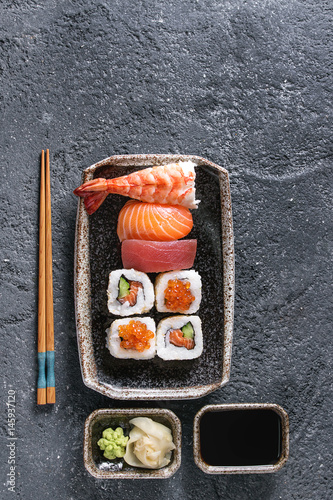 Sushi Set nigiri and sushi rolls in dark ceramic plate with soy sauce and chopsticks over black stone texture background. Top view with space. Japan menu
