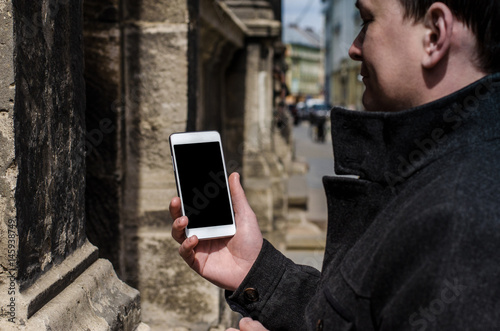 close up white mobile phone holding young hipster business man on the background of stone wall of the old city