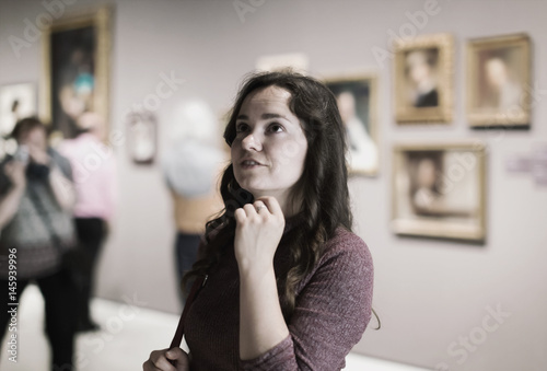 Woman attentively looking at paintings in art museum