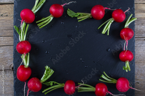 Fototapeta Naklejka Na Ścianę i Meble -  Spring fresh radishes frame  on the black slate board, top view