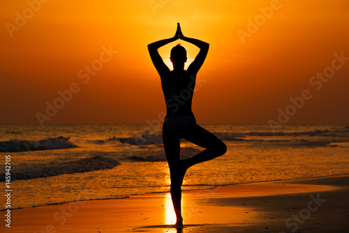 Kobieta ćwicząca jogę na plaży przy zachodzie słońca