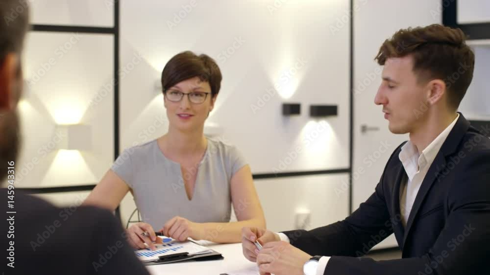 Tracking shot of beautiful businesswoman and young employee sitting at table in meeting room, smiling and speaking with coworker Tracking shot of beautiful businesswoman and young employee sitting at table in meeting room, smiling and speaking with coworker