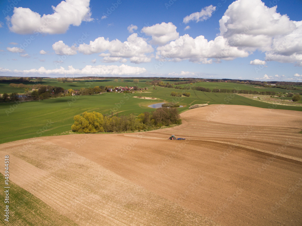 Aerial view of beautiful agricultural fields in spring with a tractor at work - tractor plough cultivating fields