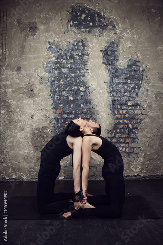 Young athletic couple practicing acroyoga. Balancing in pair. Fit active pair yoga time. Sporty handsome man supporting and holding slim beautiful brunette woman. Training time. Asana 