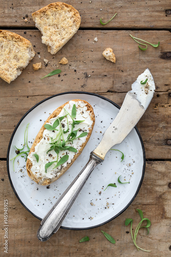 Brötchen mit Frischkäse, Kresse und Pfeffer zusammen mit einem Teller und einem Messer auf einem alten rustikalen Holzuntergrund