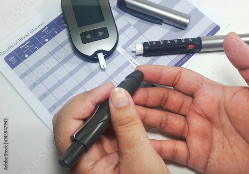 Hand doing glucose monitoring procedure using glucometer photo