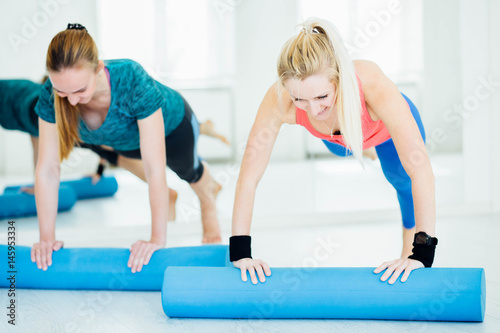 Sport and lifestyle concept. Slim fitness young girls with foam roller doing planking exercise indoors at home gymnastics.