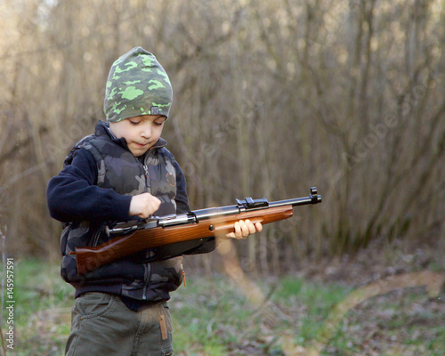Cute child in soldier uniform playing toy gun outdoors