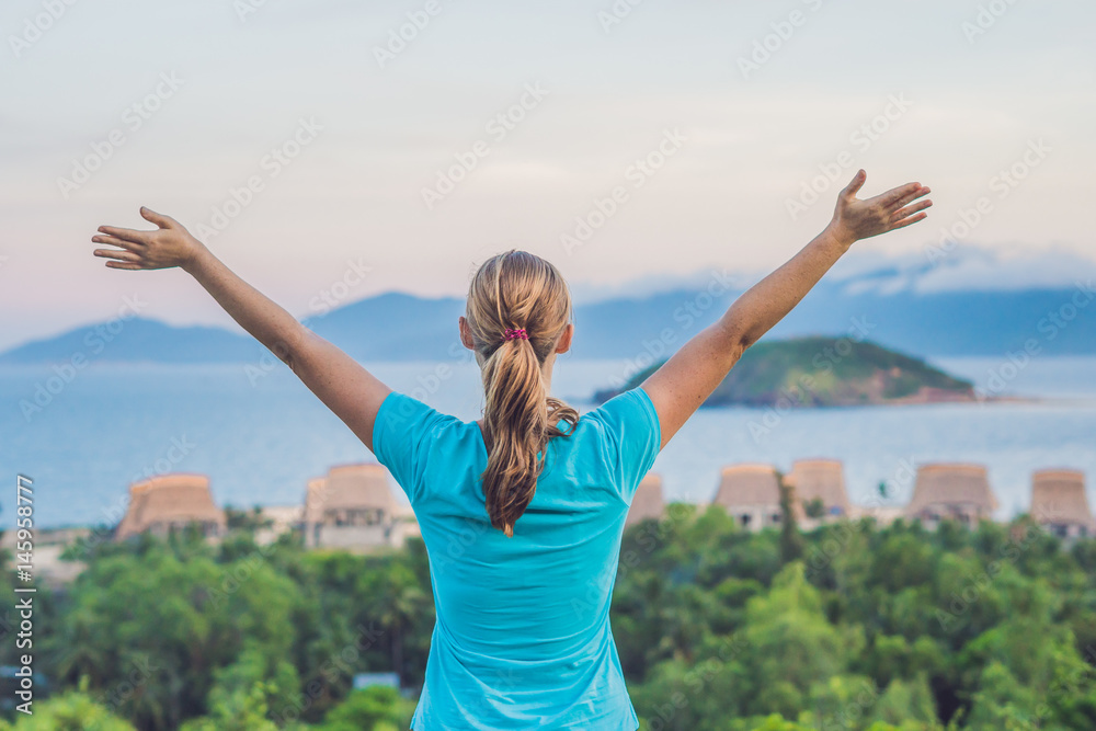 The young woman raised her hand up to the sun, against the sea, rocks and sky with clouds The young woman raised her hand up to the sun, against the sea, rocks and sky with clouds