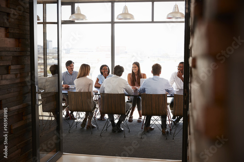 Photography Team in a boardroom meeting seen through open doors, full length