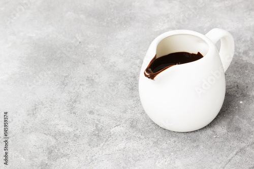 The melted chocolate (chocolate sauce) in a white sauce-boat on a light background