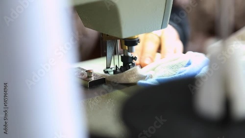 Closeup of adult female hands of seamstress at work. Woman sewing clothes for newborn babies with professional machine in factory. Real time full hd video footage. photo