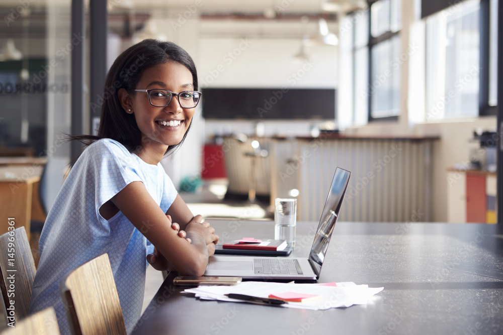 Fototapeta premium Young black woman in office with laptop smiling to camera