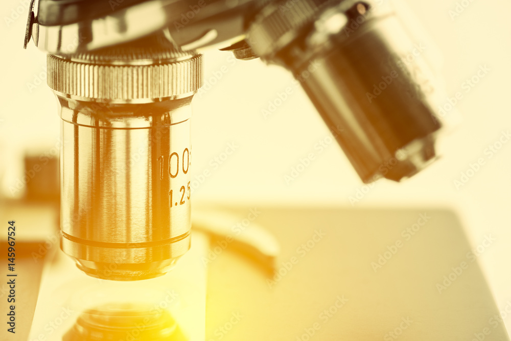 Close up of objective lenses with a microscope slide on a stage and clip. Basic optical microscopes can be very simple and there are many complex designs aim to improve resolution and sample contrast. Close up of objective lenses with a microscope slide on a stage and clip. Basic optical microscopes can be very simple and there are many complex designs aim to improve resolution and sample contrast.