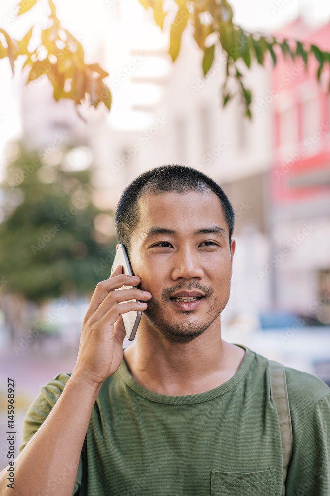 Young Asian man having a conversation on his cellphone outside Young Asian man having a conversation on his cellphone outside