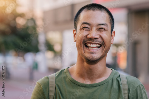 Asian man laughing while standing on a city street