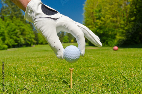 hand placing golf ball on tee over beautiful golf course with blue sky
