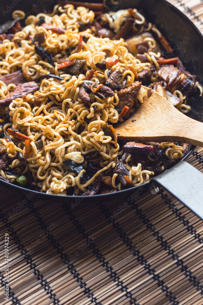 Stir fry noodles in a black pan stirred with a bamboo ladle