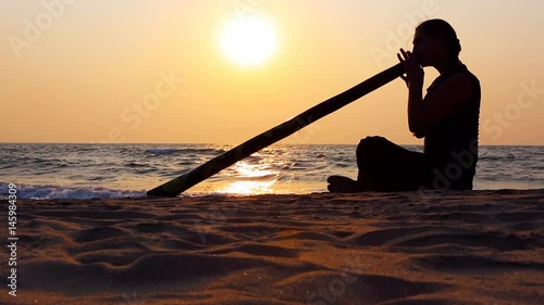 Didgeridoo playing. Male Silhouette with Didgeridu near Sea.