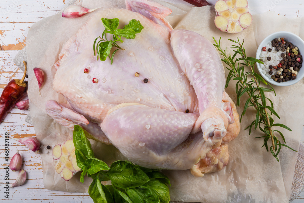 Raw whole chicken with herbs and spices on rustic wood background Raw whole chicken with herbs and spices on rustic wood background
