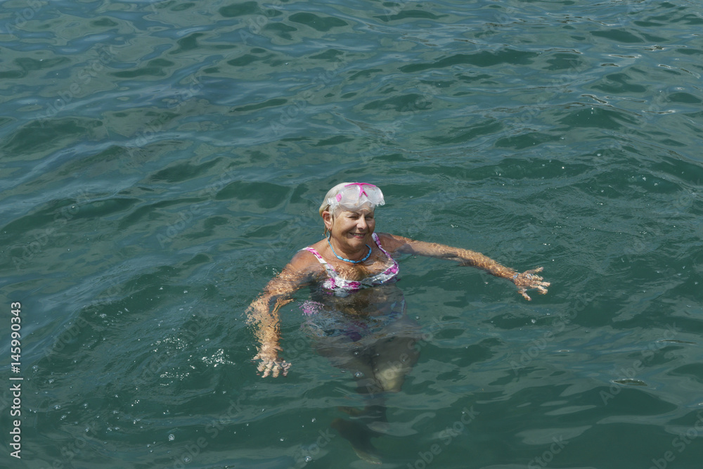 Aged woman is floating in sea water with swim mask.