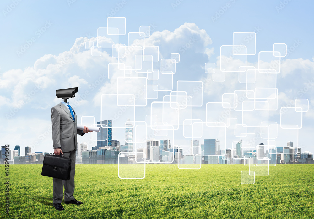 Camera headed man standing on green grass against modern cityscape