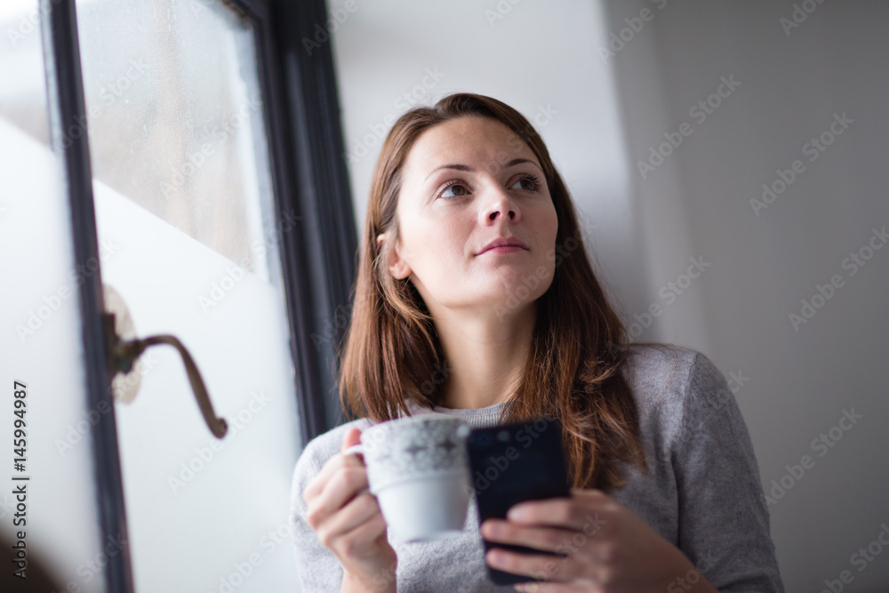 Young adult female having morning coffee and checking smartphone Young adult female having morning coffee and checking smartphone