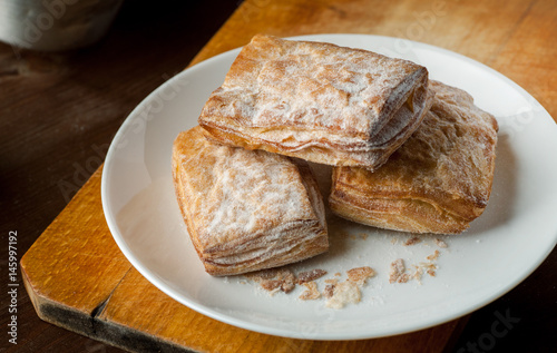 Puff pastry cookies in a white plate on a wooden cutting board