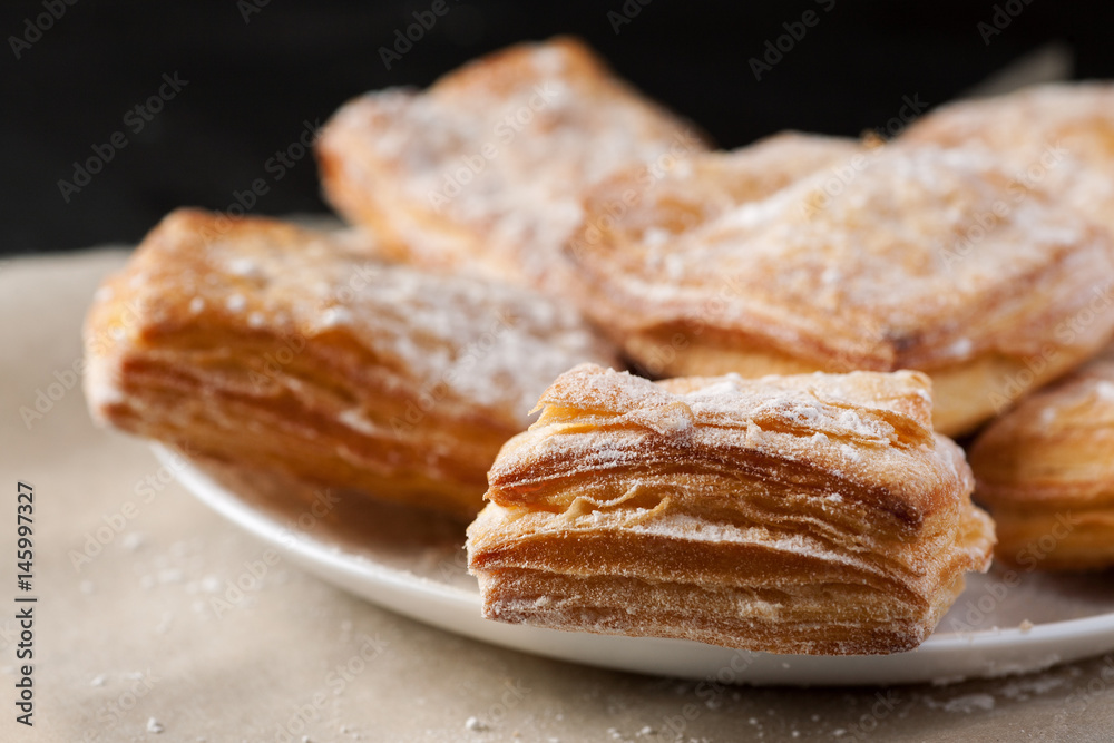 Macro shot of puff pastries dusted with powdered sugar in white plate