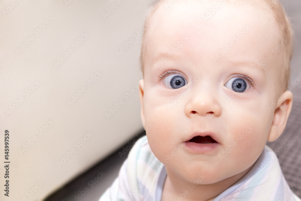 Surprised open-eyed baby boy. Close-up portrait of blue-eyed infant kid. Open-mouthed amazed toddler.