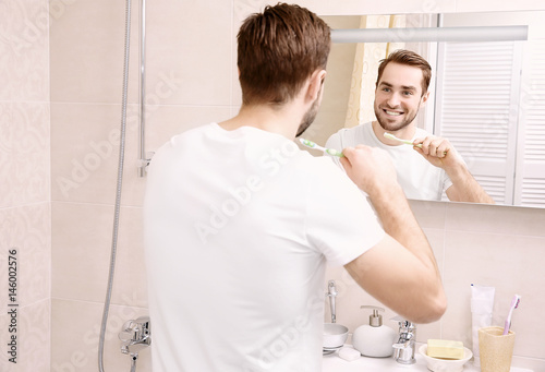 Handsome man brushing teeth in bathroom